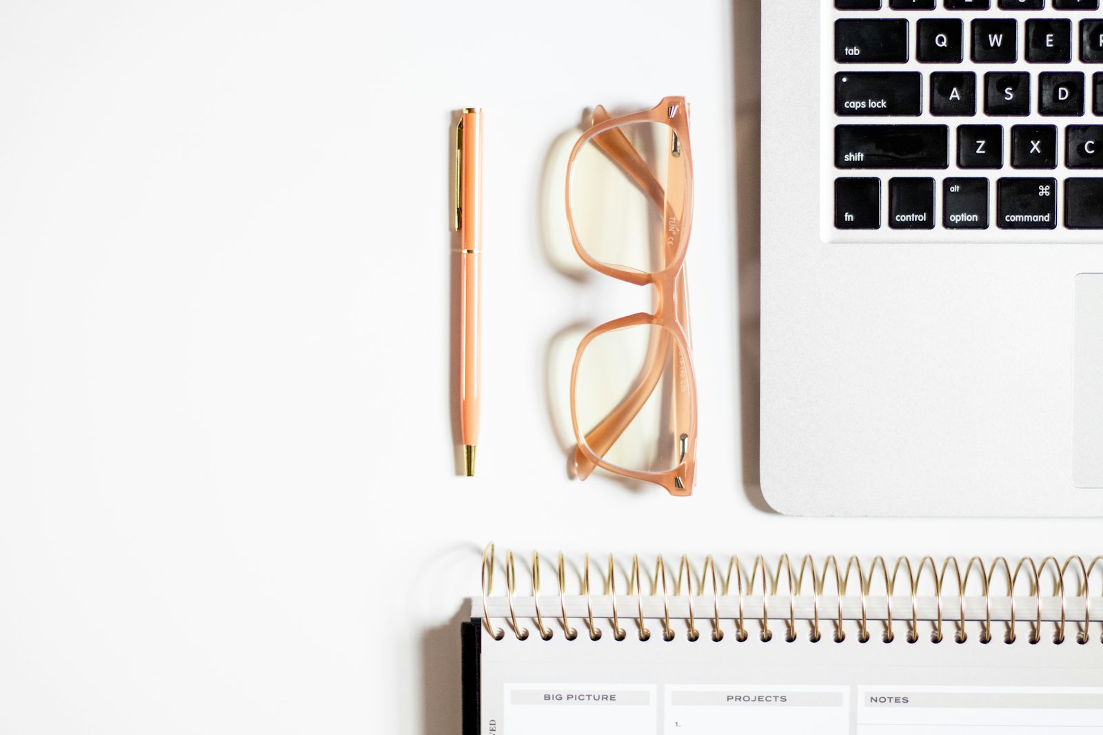 A laptop, glasses and a notepad arranged on a desk